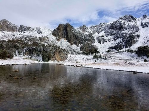Snow-capped mountains reflect in a calm lake, surrounded by a serene winter landscape.