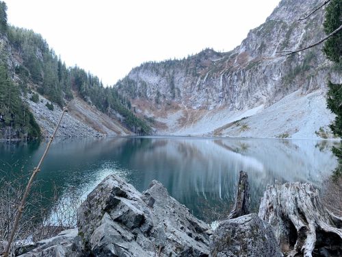 Serene lake surrounded by rocky mountains and trees, reflecting the landscape in calm waters.