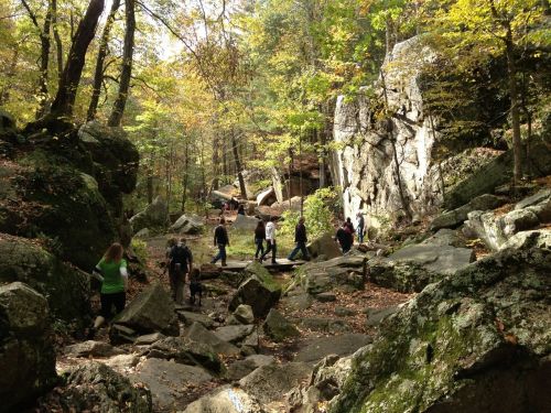 A group of hikers navigating a rocky trail surrounded by autumn foliage and large boulders.