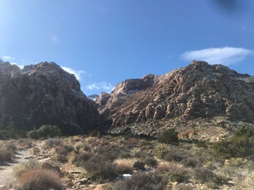 A scenic view of rugged mountains under a clear blue sky, with sparse vegetation in the foreground.