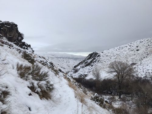 A snowy landscape with a winding path between rocky hills under a cloudy sky.