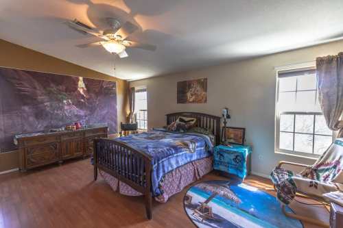 Cozy bedroom with a wooden bed, colorful bedding, a dresser, and large windows letting in natural light.