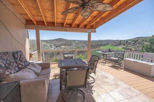 A spacious outdoor patio with a table, chairs, and a couch, overlooking a scenic landscape of hills and greenery.
