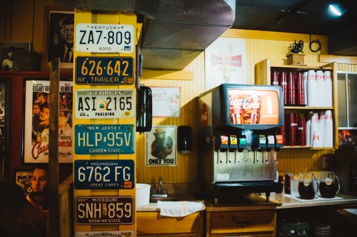 A wall adorned with vintage license plates and a Coca-Cola vending machine in a cozy diner setting.