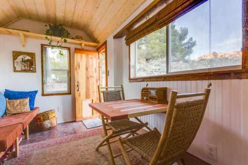 Cozy interior of a tiny home with wooden furniture, a table, and large windows letting in natural light.