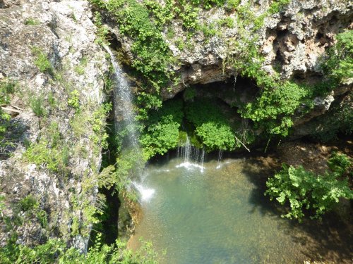 A serene waterfall cascading into a clear pool surrounded by lush greenery and rocky cliffs.