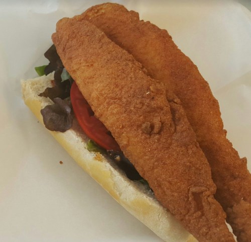 A sandwich with two crispy fried fish fillets, lettuce, and tomato on a soft hoagie roll.