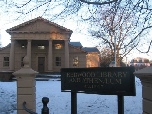 Historic Redwood Library and Athenæum building with a sign, surrounded by snow and bare trees.