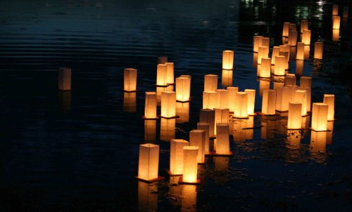 Floating lanterns illuminate a dark water surface, creating a serene and magical atmosphere.