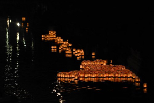 Floating lanterns illuminate a dark river, creating a serene and magical atmosphere at night.