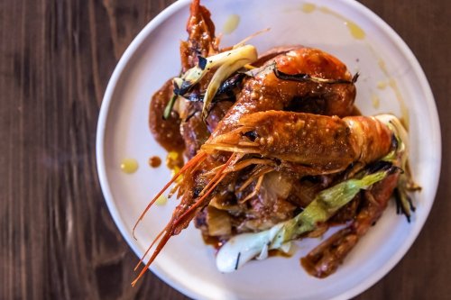 A plate of large shrimp topped with green onions and drizzled with sauce, set on a wooden table.