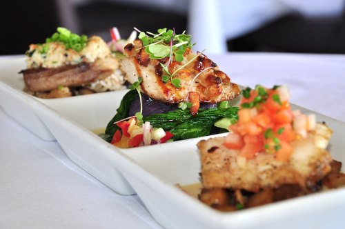 A gourmet dish featuring three portions of grilled meat, garnished with herbs and served on a white plate.