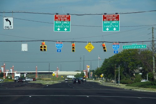 Traffic signals and road signs indicating directions for I-465/I-74, with vehicles on a multi-lane road.