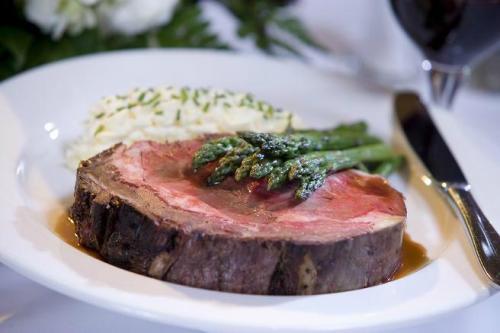 A plate of medium-rare roast beef with asparagus and creamy mashed potatoes, accompanied by a glass of red wine.