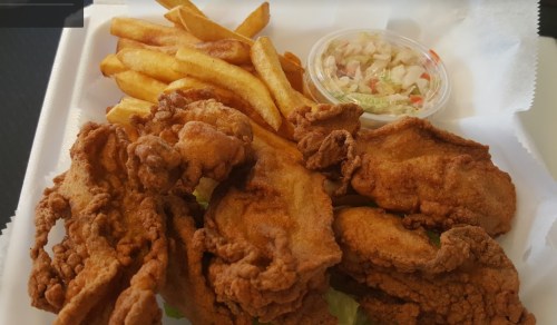 A takeout container with fried chicken, French fries, and a small cup of coleslaw on a bed of lettuce.