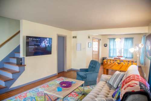 Cozy living room with a TV showing "Friends," a sofa, coffee table, and a foosball table in a bright, inviting space.