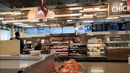 A deli counter with a menu display, showcasing sandwiches and baked goods, in a modern grocery store setting.