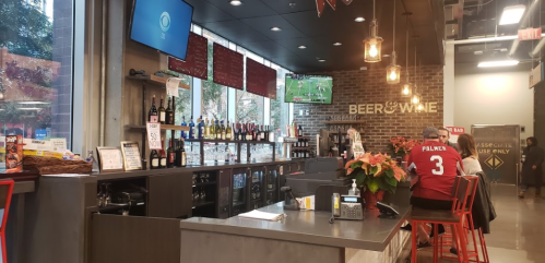 A modern bar with a variety of drinks, TVs showing sports, and a cozy atmosphere with red accents and plants.