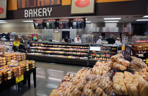 A bakery section in a store with various baked goods, including bread and pastries, and bakers working behind the counter.