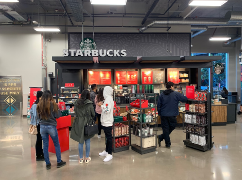 A busy Starbucks store with customers ordering at the counter and various products displayed on shelves.