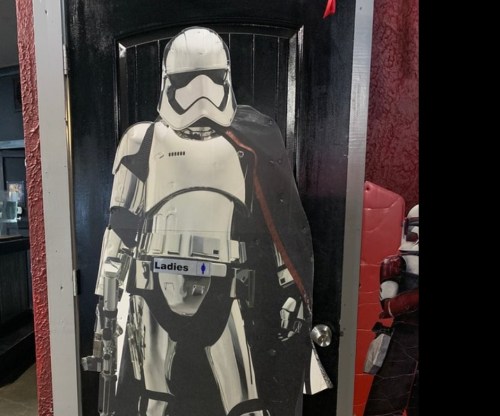 A life-sized cutout of a stormtrooper stands by a black door labeled "Ladies."