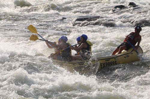 A group of people in a yellow raft navigating through turbulent whitewater rapids.