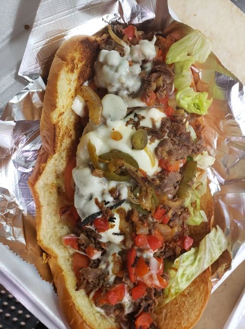 A large sandwich filled with sliced beef, lettuce, tomatoes, peppers, and creamy sauce on a toasted bun.