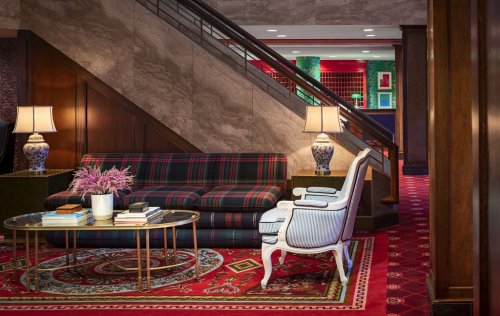 Cozy lobby area featuring a plaid sofa, white armchair, glass coffee table, and decorative lamps against a stylish backdrop.