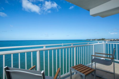 A balcony view overlooking calm blue waters and a clear sky, with two chairs and a small table.