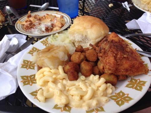 A plate of fried chicken, macaroni and cheese, okra, mashed potatoes, and a biscuit, with a side dish in the background.