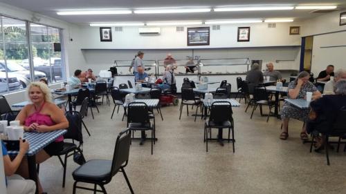 A spacious diner with checkered tables, patrons eating, and staff serving in a bright, casual setting.