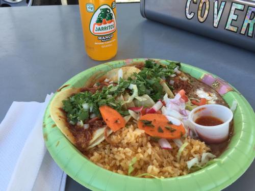 A plate of tacos topped with vegetables and sauce, served with rice and a bottle of mango Jarritos.