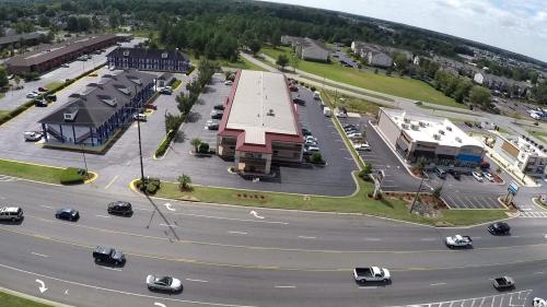 Aerial view of a commercial area with several buildings, parking lots, and a busy road lined with vehicles.