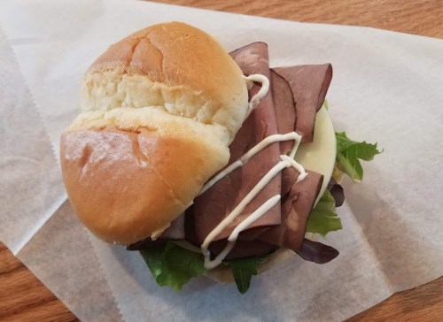 A sandwich with sliced roast beef, lettuce, and mayonnaise on a soft bun, placed on a piece of parchment paper.