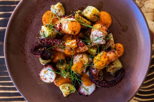 A plate of octopus with vibrant sauces, garnished with herbs and served with small potato pieces.