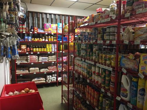 A small grocery store aisle filled with shelves of canned goods, snacks, and various food items.