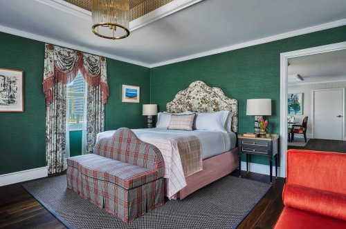 A stylish bedroom featuring a floral headboard, green walls, a patterned bench, and elegant curtains.