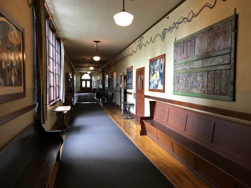 A long hallway with wooden benches, artwork on the walls, and large windows letting in natural light.