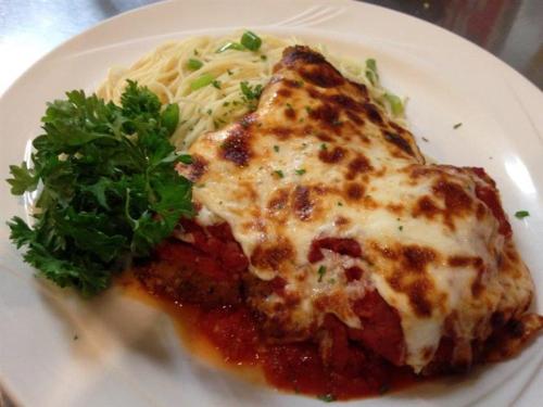 A plate of baked lasagna topped with melted cheese, served with a side of pasta and garnished with parsley.