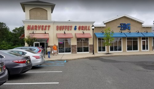 Exterior of Harvest Buffet & Grill with a parking lot, featuring a sign and nearby restaurant. Cloudy day.