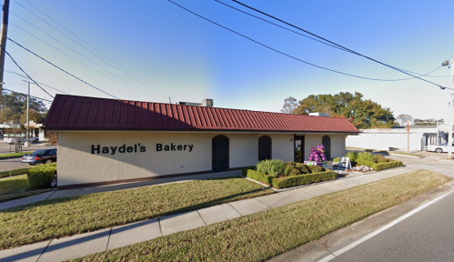 A bakery with a red roof and sign reading "Haydel's Bakery," surrounded by grass and a sidewalk.