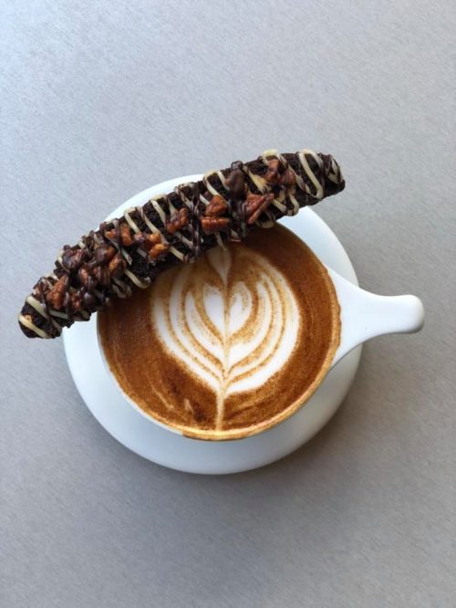 A latte with a heart-shaped foam design, topped with a chocolate-covered snack bar on the side.