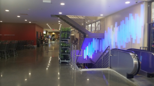 Interior of a modern store featuring an escalator, colorful wall lights, and shopping carts in the background.