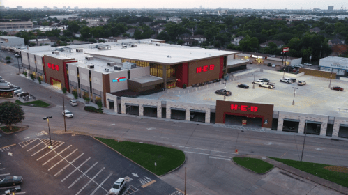 Aerial view of an H-E-B grocery store with a large parking lot and city skyline in the background.