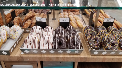 A display of assorted donuts, including glazed, chocolate-covered, and sprinkled varieties, on a wooden counter.