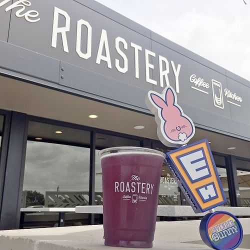 A purple drink in front of a café sign that reads "The Roastery," featuring a cute bunny decoration.