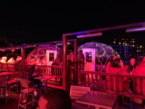 Two illuminated igloo-like structures on a rooftop bar at night, with people seated and enjoying the atmosphere.