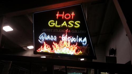 Neon sign for "Hot Glass" artist studio and gallery, featuring flames and promoting glass blowing.