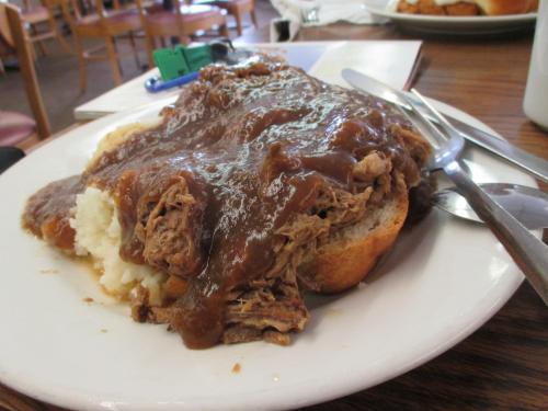 A plate of mashed potatoes topped with shredded beef and gravy, served on a slice of bread.