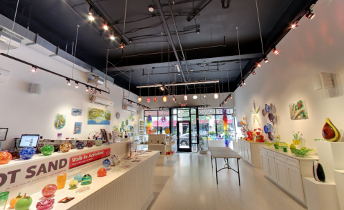 Bright art studio with colorful glass pieces displayed on walls and shelves, featuring a welcoming entrance and modern decor.